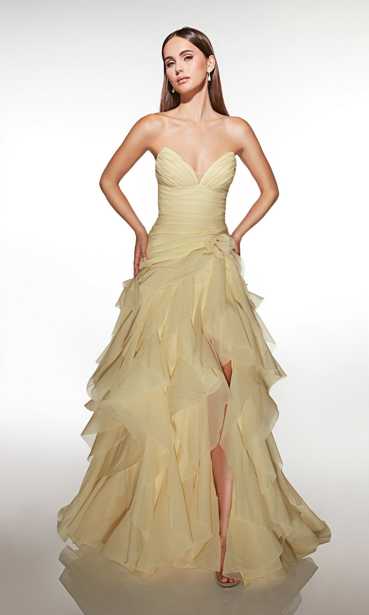 Woman wearing the Alyce 62024 long prom dress in light yellow, featuring a strapless design with ruffles and a high slit, standing against a plain white background.